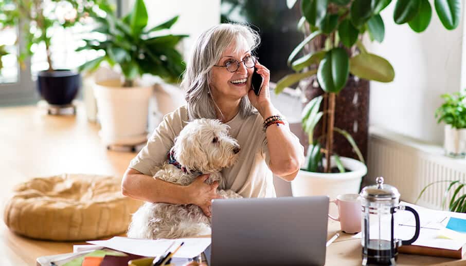 Woman sitting with her dog at her desk while talking on the phone