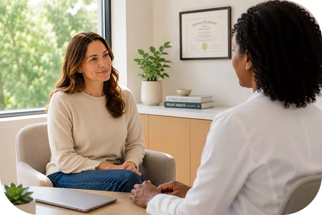 A woman in a beige sweater sits across from a doctor in a white coat during a consultation. Books labeled **"PELVIC HEALTH"** and a **University of California** diploma are visible in the background.